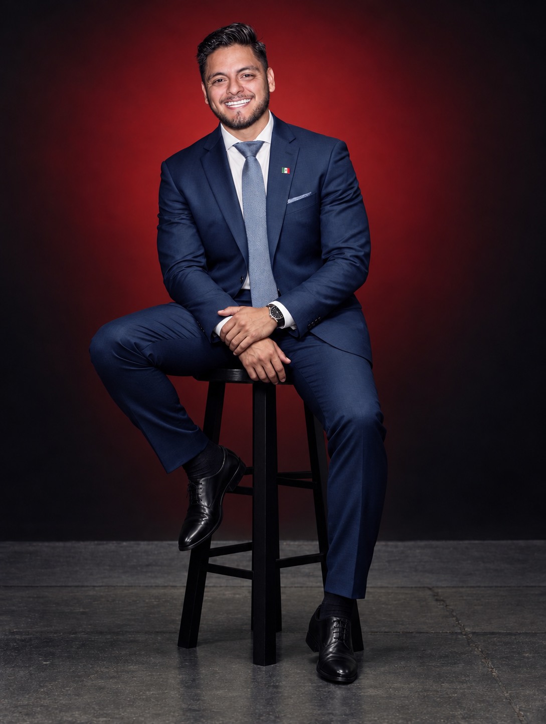 Alejandro Gómez con traje azul sobre fondo rojo y oscuro